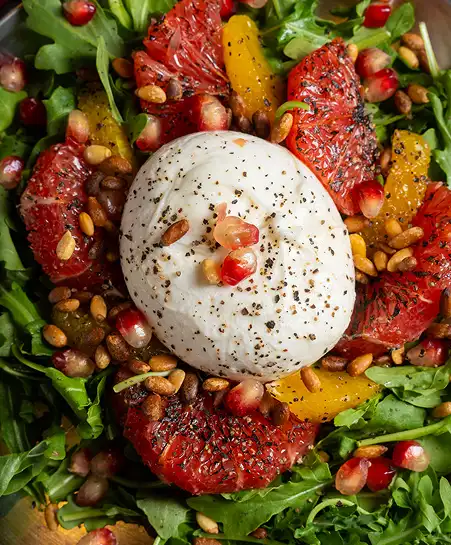 Fresh burrata cheese ball over mixed greens, blood orange and grapefruit segments, pomegranate seeds, and toasted pine nuts.