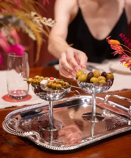 Two stainless steel cocktail dishes filled with green and black olives on a carved silver serving tray.